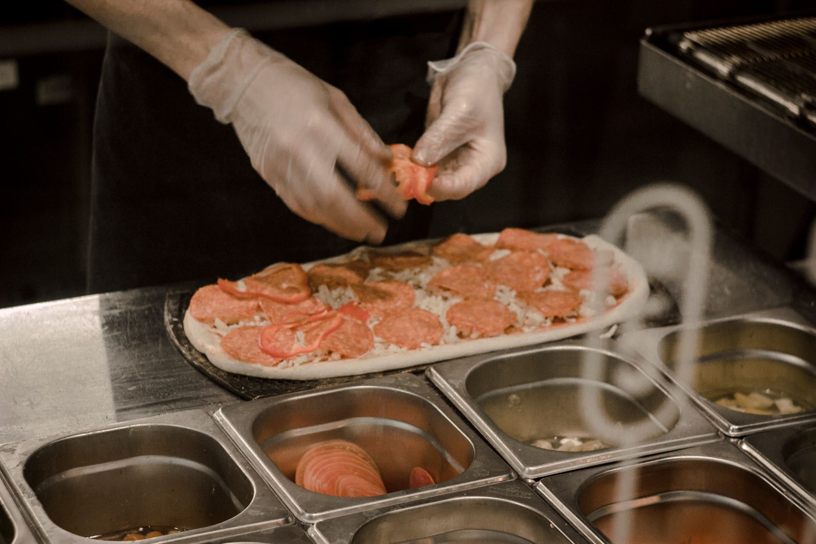 Pizza shop prep table stacked with dough, cheese, and topping trays